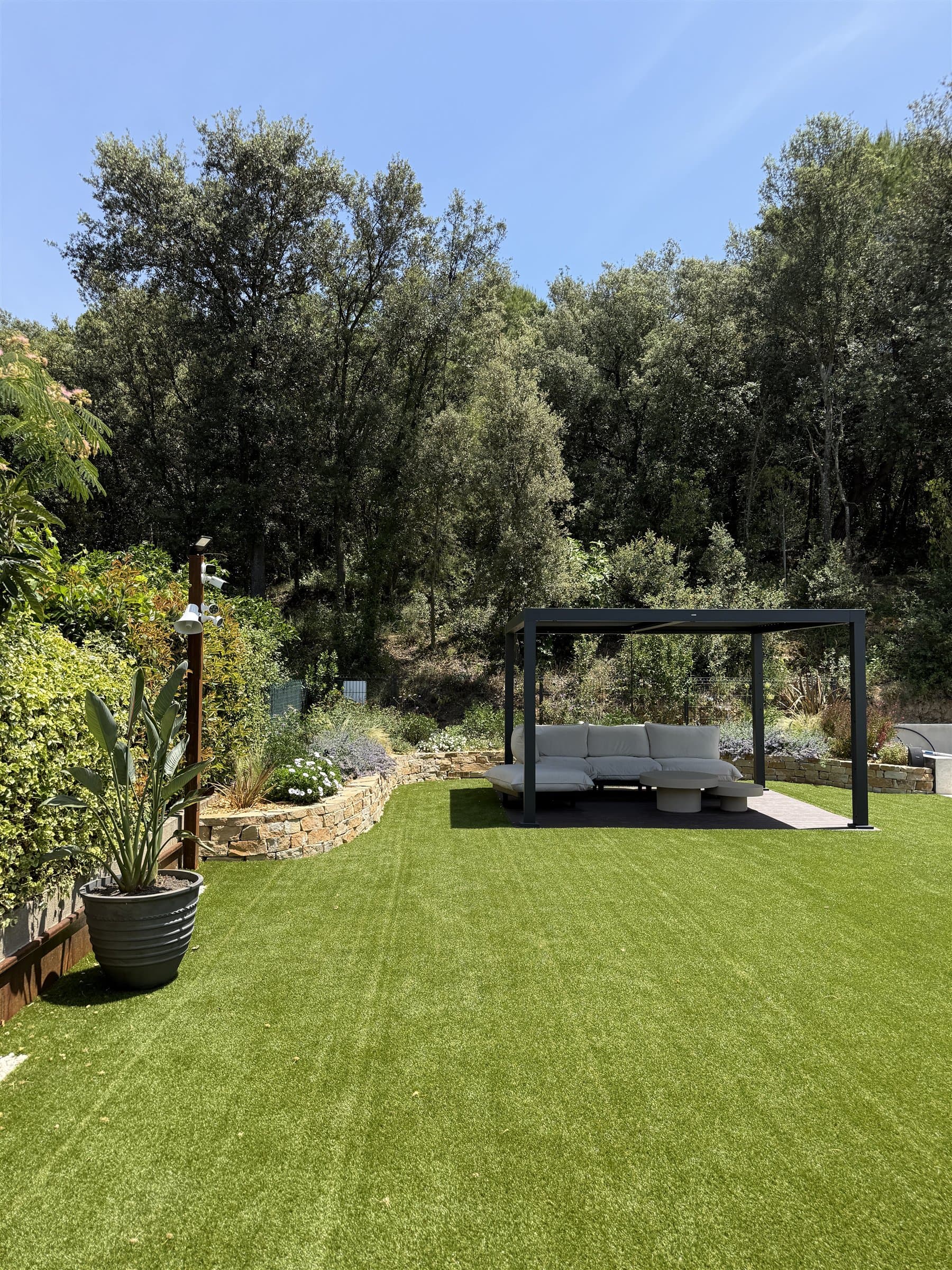 Jardí acabat amb gespa, parterres de pedra i pèrgola contemporània